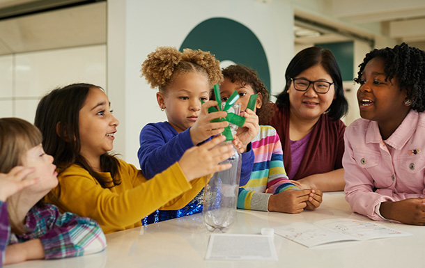 group of daisy girl scouts holding hands in uniform blue apron vest with patches and badges